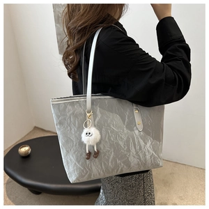 Detail of silver pleated tote bag with golden rivets and white plush monster charm