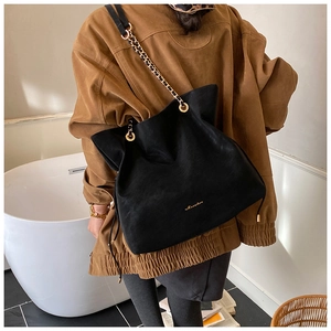 Close-up of black suede bucket bag featuring golden chain strap and brand logo