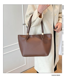 Close-up of brown leather tote bag on model showing golden metal hardware details