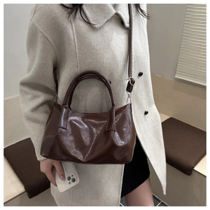 Detail of dark brown glossy leather tote bag with dual handles and crossbody strap
