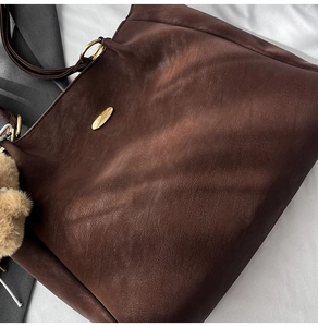 Detailed close-up of dark brown lychee texture leather tote bag with gold oval hardware