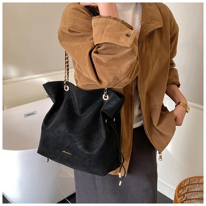 Detail view of large black bucket bag with gold chain strap and drawstring accents