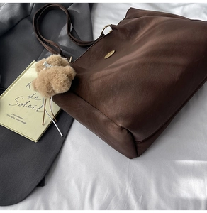 Detail of dark brown tote bag with golden metal logo and soft fuzzy keychain accessory