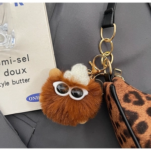 Close-up of fluffy brown pompom keychain with mini hat and sunglasses on leopard bag