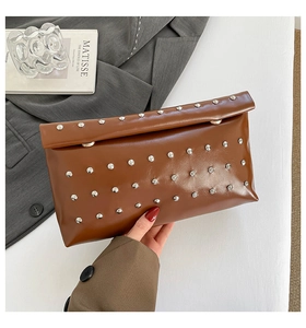 Détail d'une pochette en simili cuir caramel avec clous argentés et rabat de fermeture