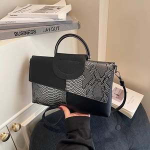 Damen Luxus Handtasche mit Schlangenmuster-Patchwork in Schwarz auf beigem Schrank