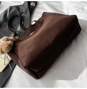 Detail of dark brown tote bag with plush ball charm on a textured leather surface
