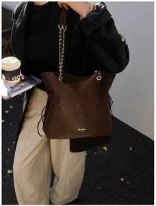 Detail of dark brown suede bucket bag with gold chain strap and drawstring side accents