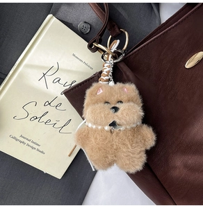 Brown plush bear keychain with pearl necklace charm on a leather tote bag