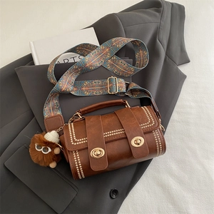 Vintage brown Boston bag with gold studs and bohemian strap on a grey blazer