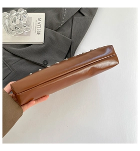 Détail d'un sac à main en cuir marron foncé avec clous argentés sur costume gris