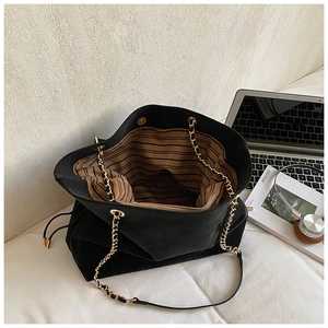 Macro detail of black suede tote bag with chain strap and striped lining interior