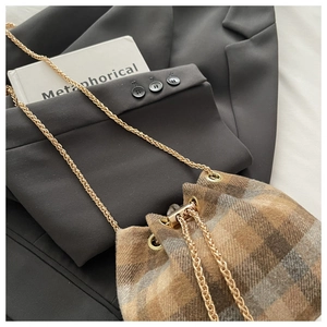 Detail of wool plaid bucket bag with gold chain strap on black blazer background