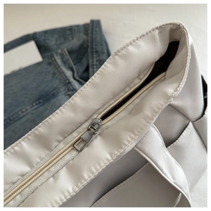 Detail of silver zipper closure and neat stitching on a white nylon shoulder bag