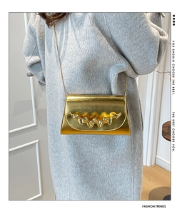 Détail du sac doré à chaîne avec garniture métallique ondulée et finition brillante sur manteau