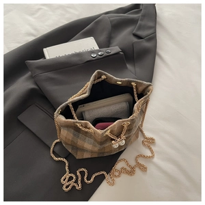 Detail of plaid wool bucket bag showing gold chain strap and pearl drawstring closure