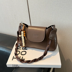 Brown leather underarm bag with woven strap and decorative wooden beads on a white book