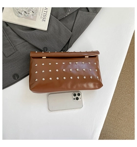 Détail du sac à main marron à rivets avec comparaison de taille par un smartphone