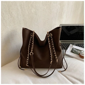 Close-up of dark brown tote bag with gold chain straps and side drawstring on an office desk