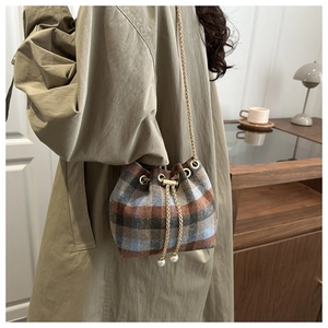 Detail of plaid bucket bag with drawstring closure, pearl accents, and gold chain strap