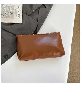 Detail of a brown glossy leather clutch bag featuring silver studs and chic urban textures