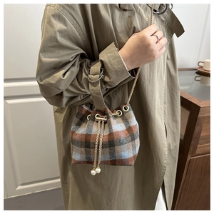 Detail of wool bucket bag with plaid pattern, gold chain strap and pearl pendant