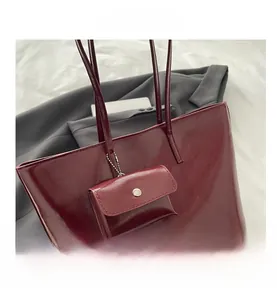 Macro view of burgundy patent leather tote showing mini charm bag and metal chain detail