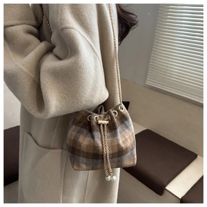 Detail of plaid wool bucket bag featuring golden chain strap and elegant pearl charms