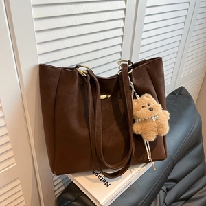 Large dark brown leather tote bag with gold metal rings and a cute plush bear pendant