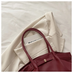 Close-up of wine red tote bag with pebble leather texture and golden buckle detail