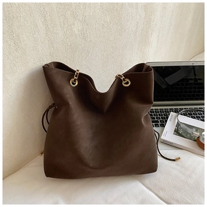 Detail of dark brown tote bag with gold chain handle and matte texture on a desk
