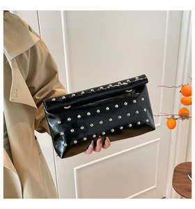 Detail of black glossy envelope clutch bag with silver metal studs in model's hand