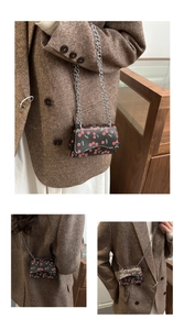 Detailed view of black crossbody bag with cherry print and silver chain strap