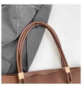 Detail of brown tote bag handle with gold hardware on a grey blazer for workplace style