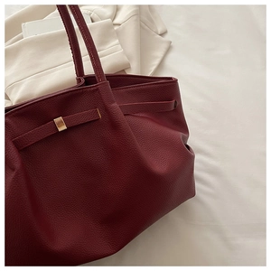 Detail of burgundy tote bag with litchi texture on white bedding with a blazer