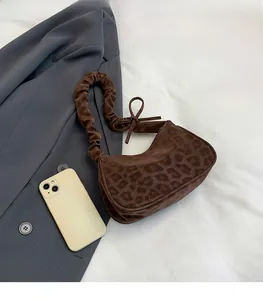 Dettaglio borsa leopardata con tracolla arricciata e fiocco accanto a uno smartphone