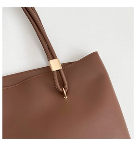 Detailed close-up of light gold metal hardware and stitching on a brown leather tote bag