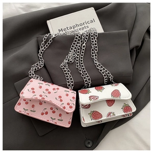Close-up of two mini crossbody bags with cherry and strawberry prints on a grey blazer