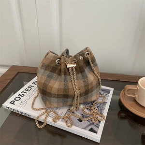 Fashionable plaid drawstring bucket bag with gold chain strap on a wooden table