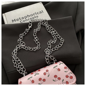 Pink shoulder bag with cherry print and bold silver chain on a black background