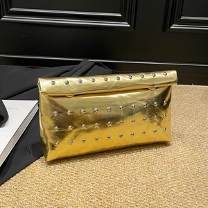 Pochette dorée chic avec clous argentés et fermoir métallique sur un tapis texturé