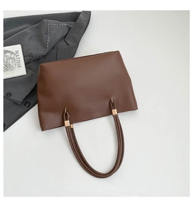 Detail of dark brown tote bag featuring golden metal buckles and smooth synthetic texture