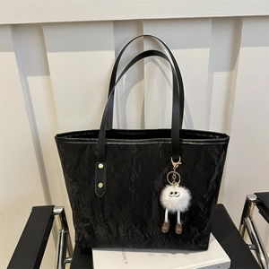Minimalist black tote bag with textured finish and cute plush doll pendant on white books