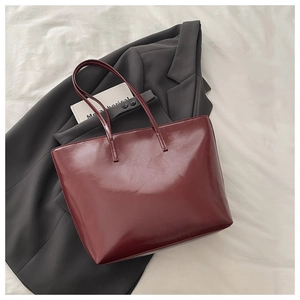 Close-up of a large burgundy tote bag in glossy faux leather on a grey suit jacket