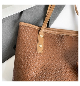 Detailed close-up of brown embossed leather texture and gold hardware on tote bag