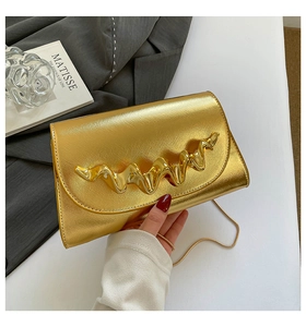 Détail du sac boîte doré avec ferrures métalliques ondulées et fini texturé sur un bureau