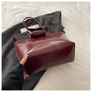 Detail of burgundy glossy leather tote bag with matching mini charm on grey blazer