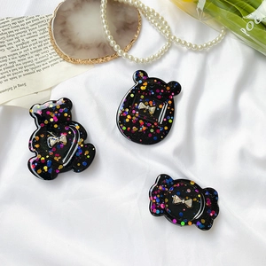 Detailed view of glittery acrylic phone grips in bear and heart shapes on white silk