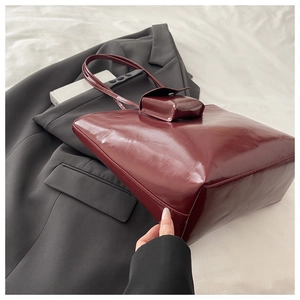 Detail of burgundy soft leather tote bag with matching mini pouch on a grey suit jacket