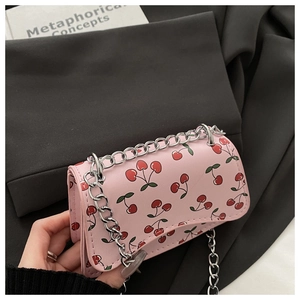 Pink cherry print crossbody bag with silver chain strap held against dark backdrop